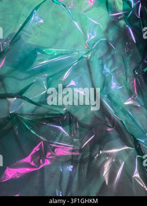 Abstract background texture featuring crumpled transparent plastic film illuminated by vibrant pink and green studio lights. Reflections and shadows c Stock Photo