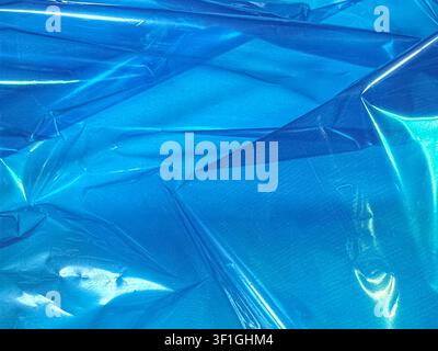 Crinkled blue plastic sheeting creates textural abstract background with strong highlights and shadows. Bright, reflective surface with deep blue tone Stock Photo