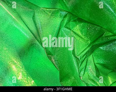 Close up texture view of crumpled green shiny fabric with small water droplets reflecting light. Vibrant emerald green color gradient, highlighting th Stock Photo