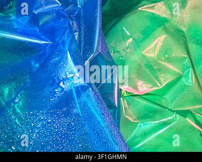 Textured crumpled plastic film in vibrant blue and green hues, dappled with moisture droplets, creating abstract patterns and shimmering highlights. C Stock Photo