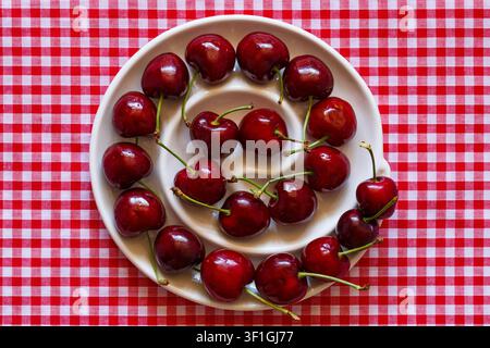Swirl of British red cherries in bowl on red and white gingham cloth, British red cherries sweet & juicy Penny variety from Kent UK from M&S Stock Photo