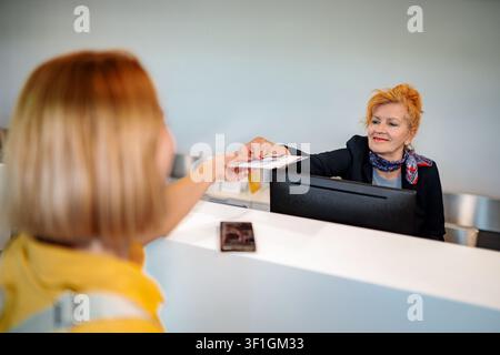 Customer checking in at reception desk passing documents to employee Stock Photo