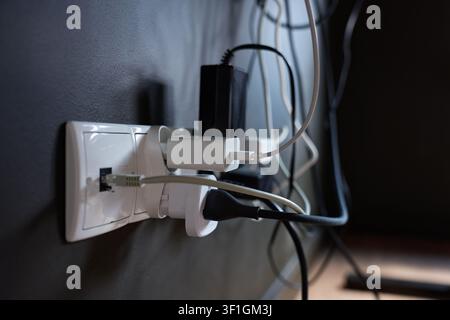 Wall outlet with multiple power adapters, plugs and connected cables for electronic devices. Concept of power supply and cable management Stock Photo