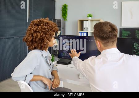 Developers discussing code on monitors, mentor pointing and explaining solutions Stock Photo