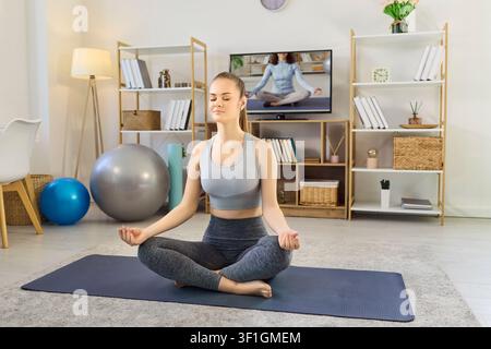 Woman meditating at home with yoga class on TV, practicing mindfulness and fitness Stock Photo