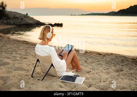 Woman using tablet at beach charging with portable solar panel Stock Photo