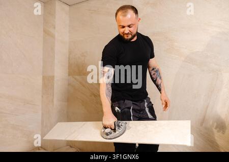 Professional tiler working on a new bathroom, installing large format tiles on the wall using a suction cup for heavy lifting Stock Photo