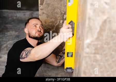 Builder checking the evenness of marble tiles with a level tool, ensuring precision and accuracy during renovation work on a wall Stock Photo