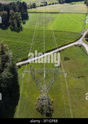 Power lines stretch across fields and rural land under a clear blue sky. Towers support the electrical grid for energy supply. Stock Photo