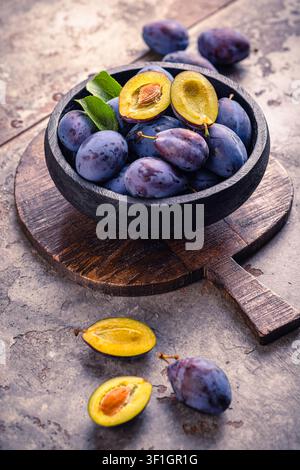Fresh ripe plums in a rustic bowl on a wooden board, a healthy fruit snack Stock Photo