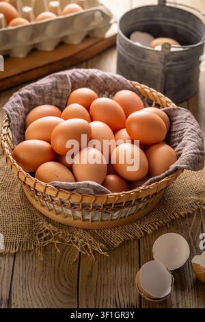 Basket full of fresh brown eggs on a rustic wooden table with a whisk and shell fragments Stock Photo
