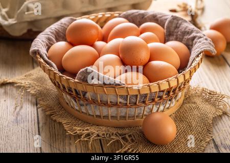 Basket full of fresh brown eggs on a rustic wooden table with a whisk and shell fragments Stock Photo