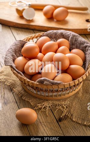 Basket full of fresh brown eggs on a rustic wooden table with a whisk and shell fragments Stock Photo