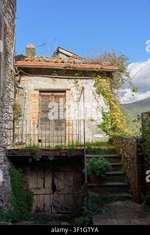 Vertical shot of a charming weathered stone house with overgrown green ivy on a terracotta tile roof, an old wooden balcony door, a rustic basement, a Stock Photo