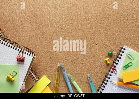 Notepads, pencil, sticky notes, paper sheets, paper clips and binder clips  on cork board  with copy space for text.  Top view of colorful school supp Stock Photo