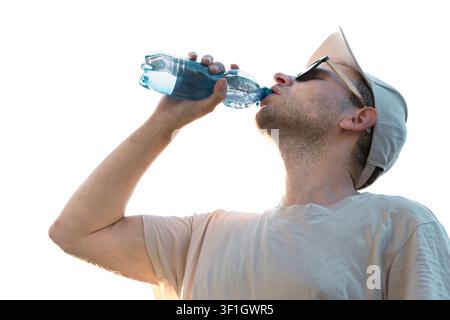 Young man wearing a cap and sunglasses drinking water from a plastic bottle, illustrating hydration and heat safety. Stock Photo