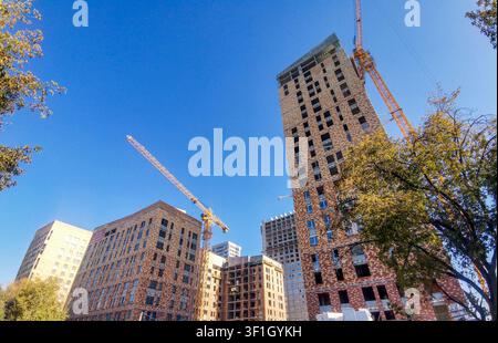 Construction site featuring several buildings in various stages of completion, with cranes and trees visible under a clear blue sky Stock Photo