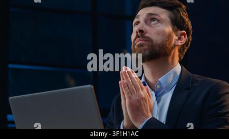 Caucasian middle aged business man wishing hoping praying with computer at dark night office adult 40s businessman male entrepreneur manager with hope Stock Photo