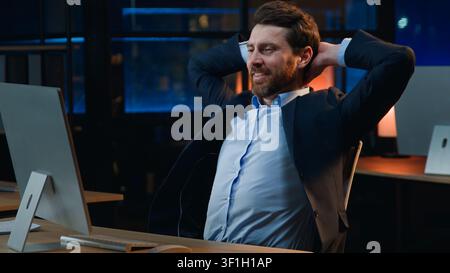 Happy middle-aged Caucasian business man finishing work with computer relaxing in night evening office businessman male employer working accomplish Stock Photo