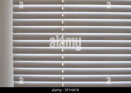 Close up background of dusty white plastic venetian blinds. Horizontal window slats with cord thread slots covered in dust layers inside office or apa Stock Photo