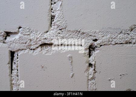 Grungy painted block wall background. Close up texture of white concrete bricks with messy mortar layers, uneven surface, and cracks in building const Stock Photo