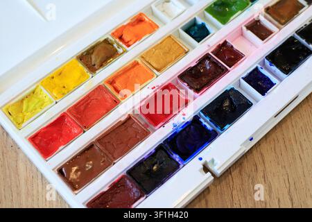 Close up texture of vibrant watercolor paint pans inside white plastic tray box. Artistic craft set layout on wooden table surface indoor Stock Photo