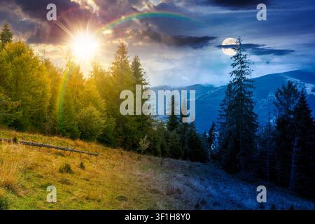 mountain landscape ukraine with spruce forest. day meet night. sun and moon over rural valley of podobovets in the distance. epic sky. equinox backgro Stock Photo