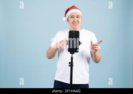 Young man wearing a red santa hat holding smartphone on stabilizer Stock Photo