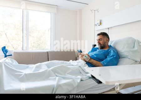 Patient using smartphone in hospital bed recovering Stock Photo