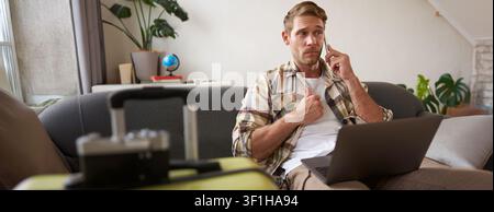 Portrait of man talking on mobile phone, tourist with laptop and suitcase answers telephone. Stock Photo