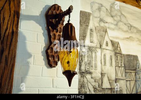This beautiful interior design photograph captures a unique vintage wall lamp hanging on a painted white brick wall. The rustic lantern is made of dark carved wood with a beautifully shaped bracket Stock Photo