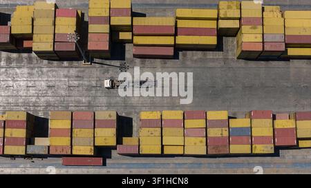 An aerial shot of cargo containers lined up in neat rows in the logistics area of a container port, with an empty tractor-trailer parked in the center Stock Photo