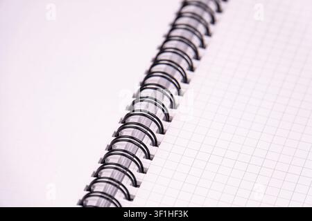 Close-up spiral notebook with grid pages, focusing on binding detail, emphasizing paper texture, studio lighting, clean composition, white and black c Stock Photo