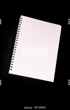 Spiral-bound notebook on graph paper against black background, presenting clean structured appearance, dynamic diagonal placement, even soft lighting, Stock Photo
