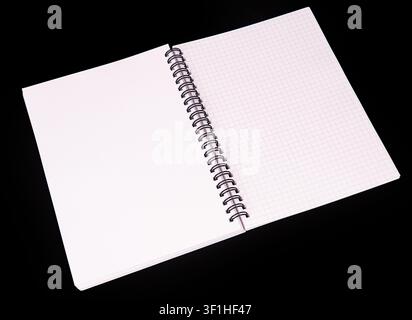 Minimalist spiral notebook with graph paper, positioned diagonally against black background, emphasizing white pages, grid pattern, smooth texture, me Stock Photo