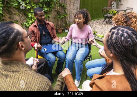 Diverse people participating in an outdoor group therapy session, sitting in a circle, holding hands, and sharing experiences, symbolizing support, co Stock Photo