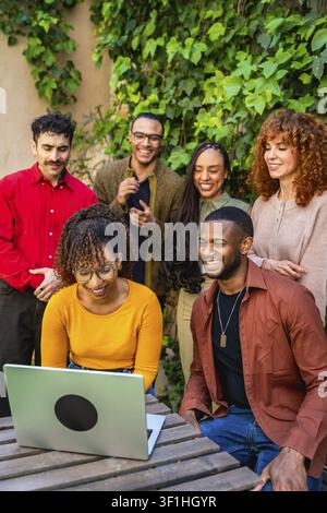 Group of diverse people collaborating and communicating during an outdoor therapy session, viewing information together on a laptop with smiles, embod Stock Photo