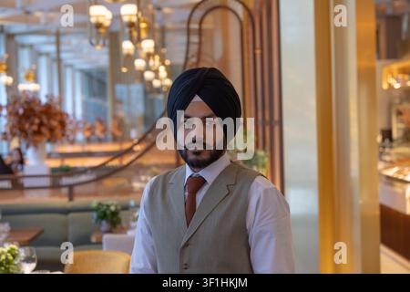 Portrait of a professional Indian Sikh hospitality worker wearing a traditional turban, standing inside a luxury hotel fine-dining restaurant Stock Photo