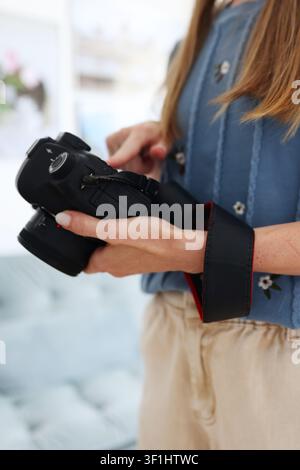 Female photographer checking camera controls before a photoshoot, close-up of hands with professional digital camera indoors. Stock Photo