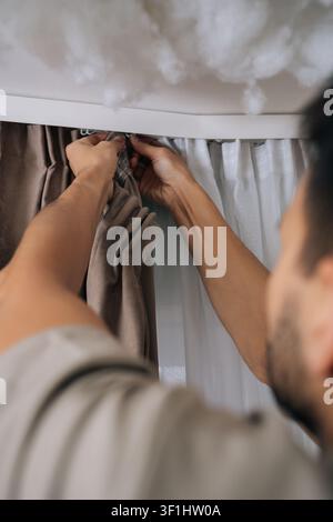 Close-up of man hanging curtains on modern curtain rail, installing new window treatments in stylish bedroom, engaging in home improvement and Stock Photo