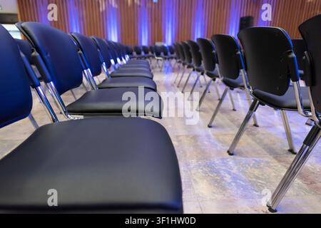 Rows of black conference chairs arranged in a modern event hall before a business conference, seminar or corporate meeting. Stock Photo