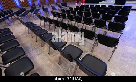 High-angle view across rows of empty conference chairs arranged on both sides of an aisle in a meeting hall. Stock Photo