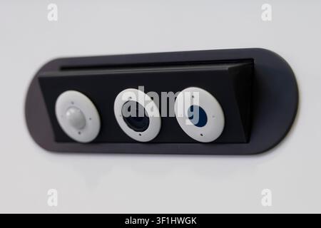 Close-up of a wall-mounted security sensor with three circular modules in a dark rectangular housing. Stock Photo