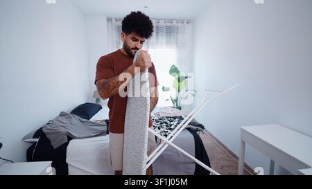 Young man setting up an ironing board while doing chores at home Stock Photo