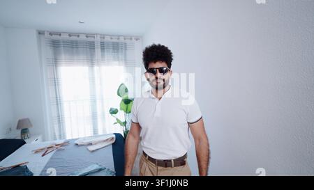 Stylish man in sunglasses standing in a bright modern bedroom Stock Photo