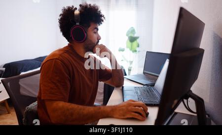Young man studying remotely at home across multiple screens Stock Photo
