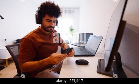 Professional man in a headset using a smartphone while working from home Stock Photo