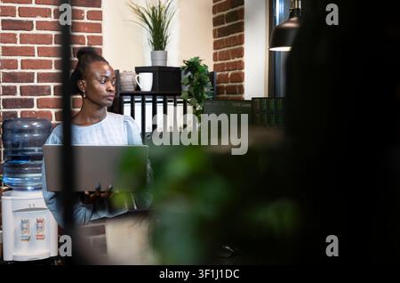 Forex Manager Reviewing Financial Screens with Laptop while a laptop and multiple monitors show forex data, currency exchange status and financial analysis for business investment work. Stock Photo