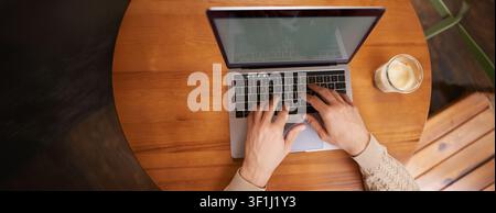 Close up portrait of male hands typing on keyboard, working on laptop in cafe, computer and cappuccino standing on wooden table in coworking space. Stock Photo