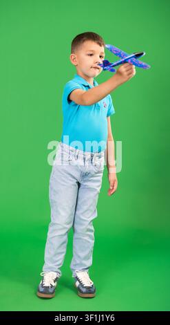 Boy in blue jeans playing with airplane model on green background Stock Photo